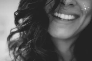 Photo noir et blanc du sourire d'une femme brune accompagné du halo blanc du logo d'Oser Demain
