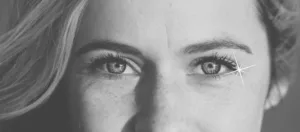 Photo en noir et blanc du visage d'une femme qui nous regarde dans les yeux avec gentillesse, le visage et illuminé par une lumière naturelle